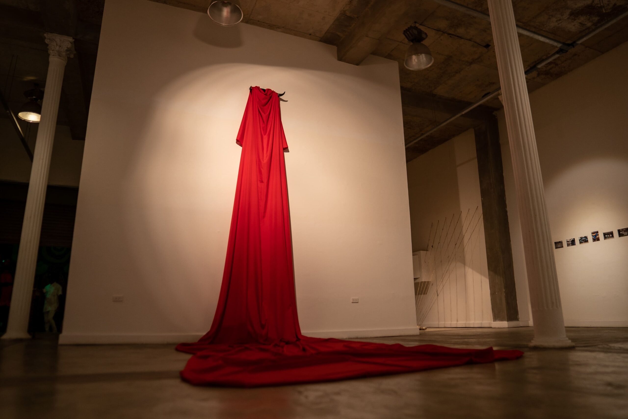 En el trabajo, one observes an installation composed of a long red fabric that falls vertically from a raised point on the wall and extends onto the floor. At the upper part, the fabric appears to be suspended by bull horns, which emerge as both a support and a symbolic element of the piece. José Miguel Cano - Statu Quo / instalación / bull horns and fabric / variable dimensions / 2023